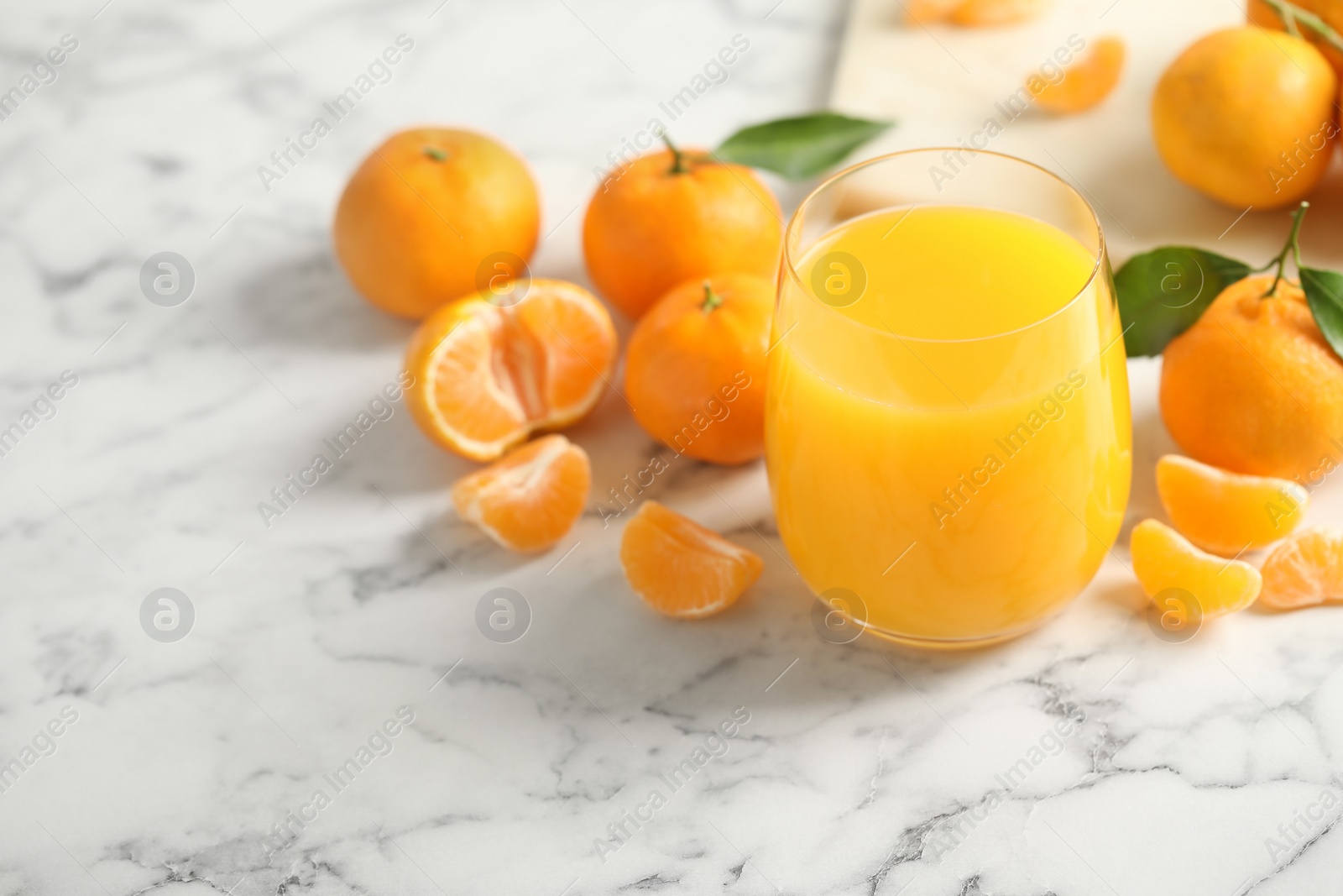 Photo of Glass of fresh tangerine juice and fruits on marble table. Space for text