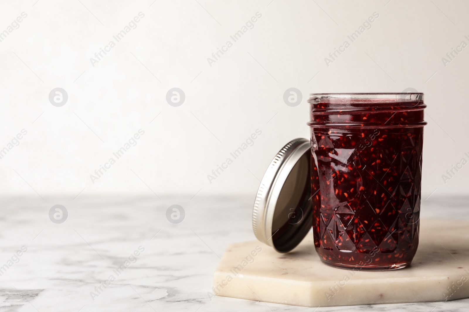 Photo of Delicious raspberry jam on marble table. Space for text