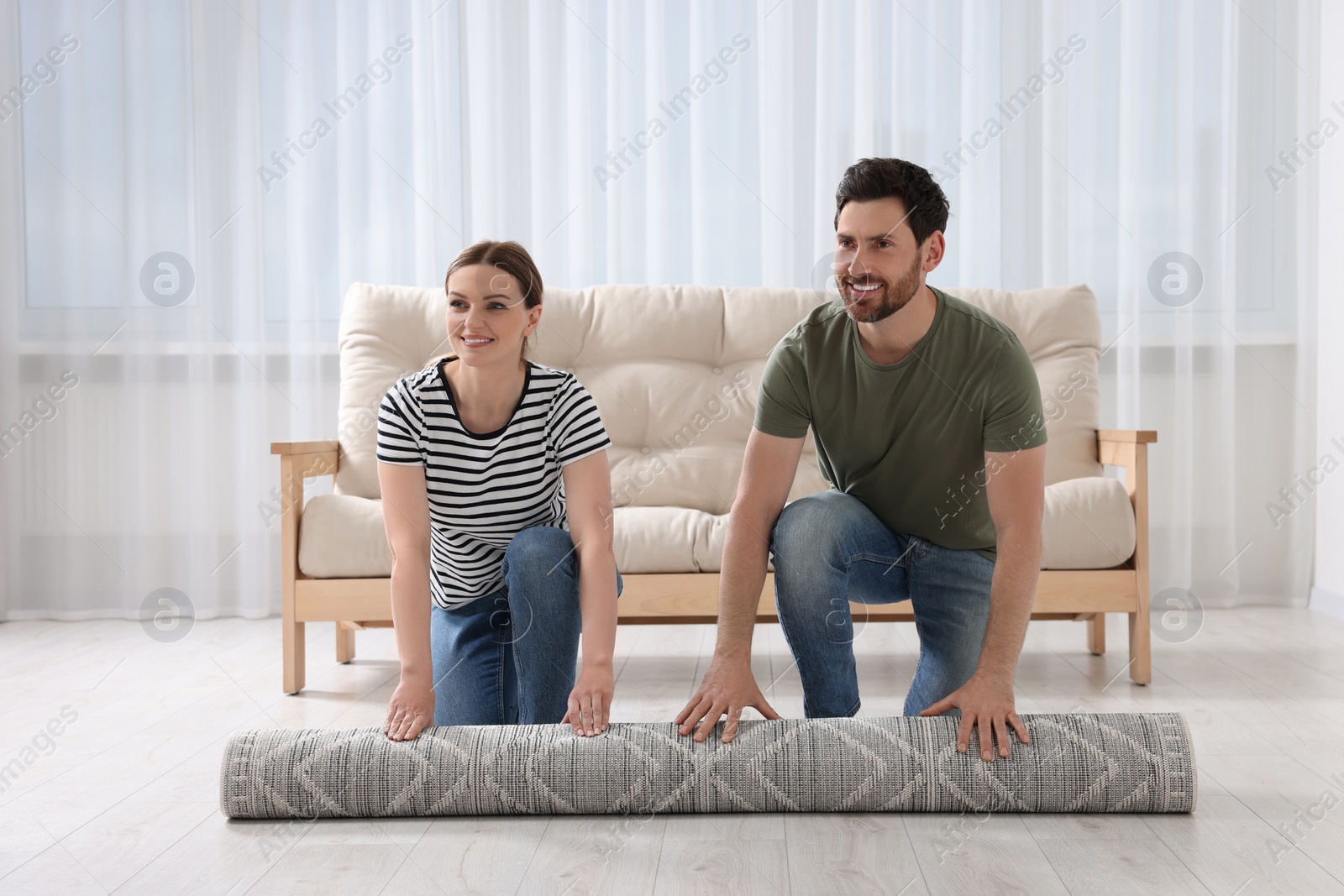 Photo of Smiling couple unrolling carpet with beautiful pattern on floor in room