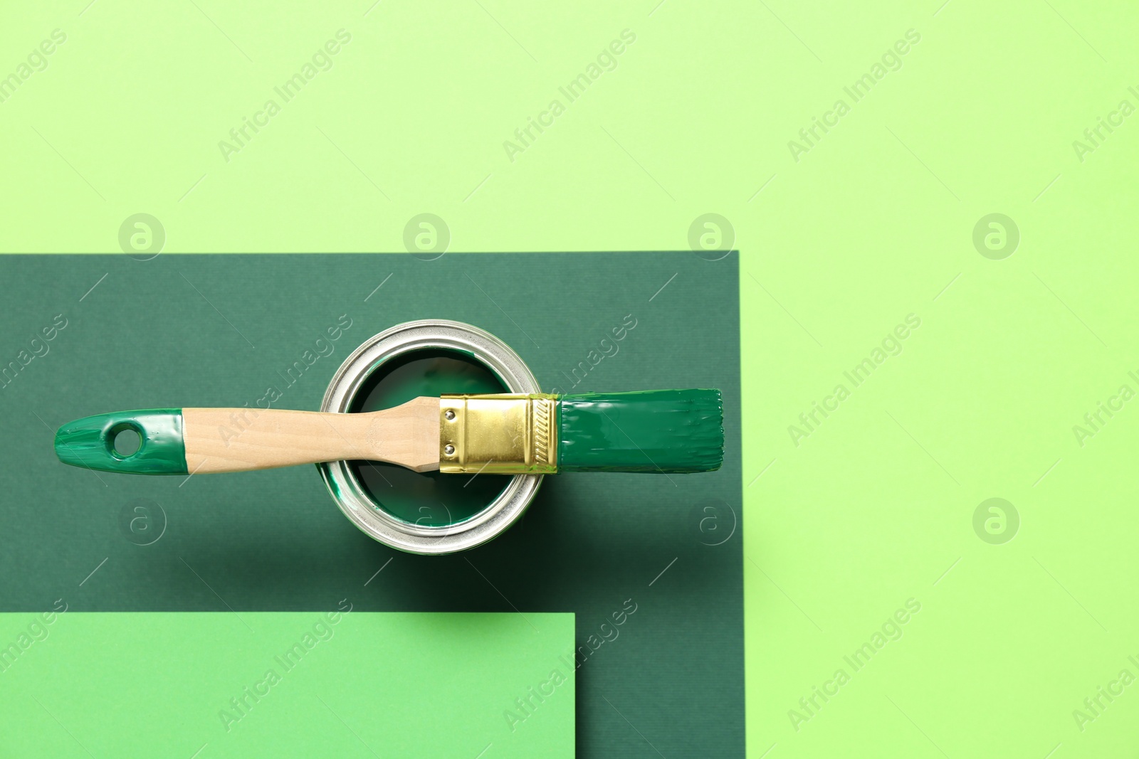 Photo of Can of green paint with brush on color background, top view. Space for text