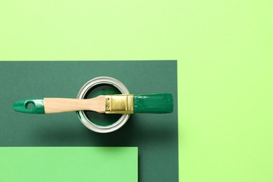 Can of green paint with brush on color background, top view. Space for text