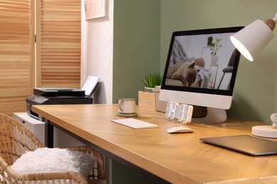 Photo of Stylish workplace with computer, laptop and lamp near olive wall at home