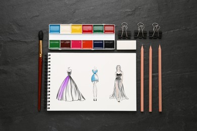 Sketches of different clothes in pad on black table. Fashion designer's desk with stationery, flat lay