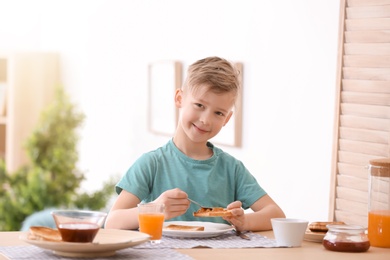 Photo of Cute little boy spreading jam onto tasty toasted bread at table