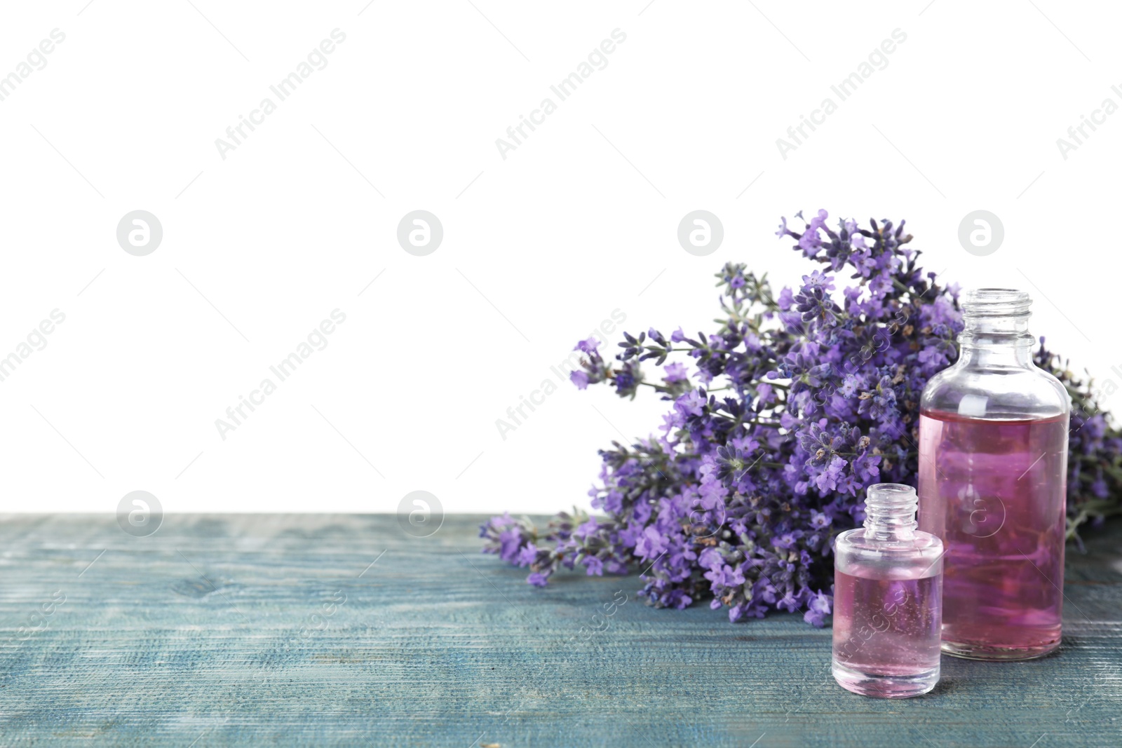 Photo of Bottles of essential oil and lavender flowers on blue wooden table against white background
