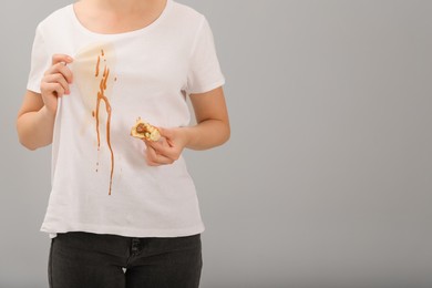 Photo of Woman holding pastry and showing stain from condensed milk on her shirt against light grey background, closeup. Space for text