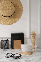 Photo of Stylish office workplace. Decor elements, glasses, cup and stationery on marble table near white wall