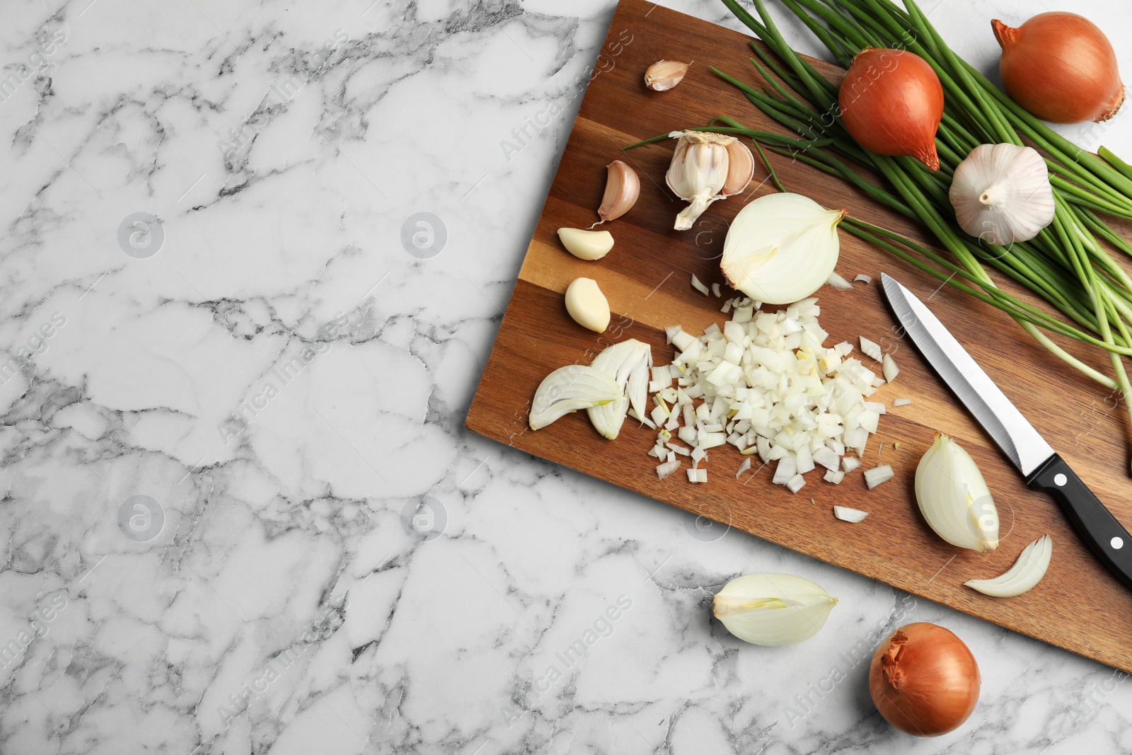Photo of Board with cut onion and garlic on marble table, top view. Space for text
