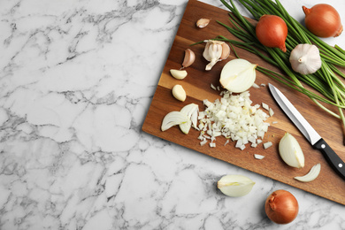 Photo of Board with cut onion and garlic on marble table, top view. Space for text