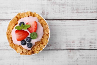 Delicious crispy cornflakes, yogurt and fresh berries in bowl on white wooden table, top view with space for text. Healthy breakfast
