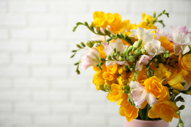 Beautiful blooming freesias in vase against white brick wall. Space for text