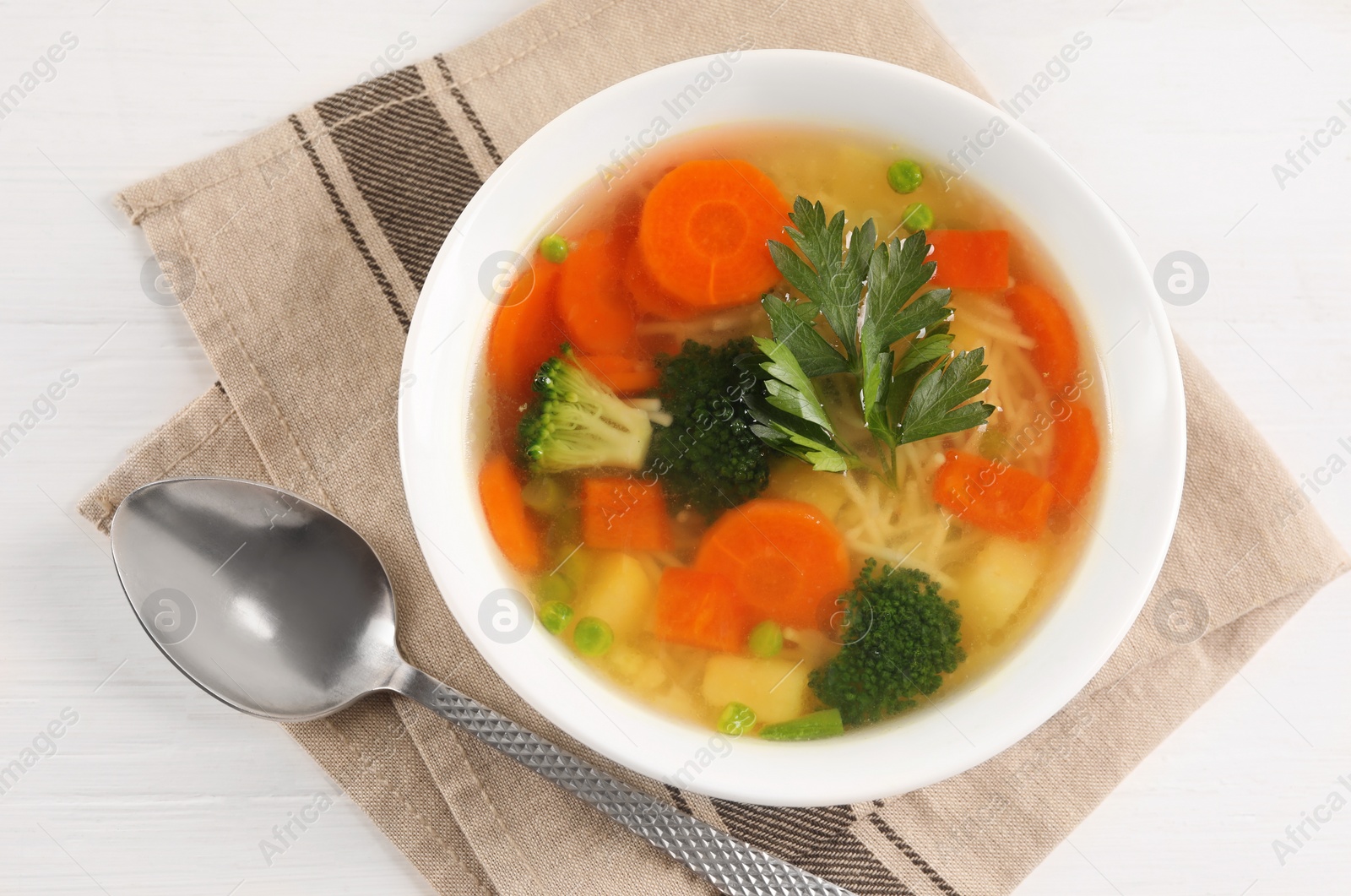 Photo of Delicious vegetable soup with noodles and spoon on white wooden table, top view