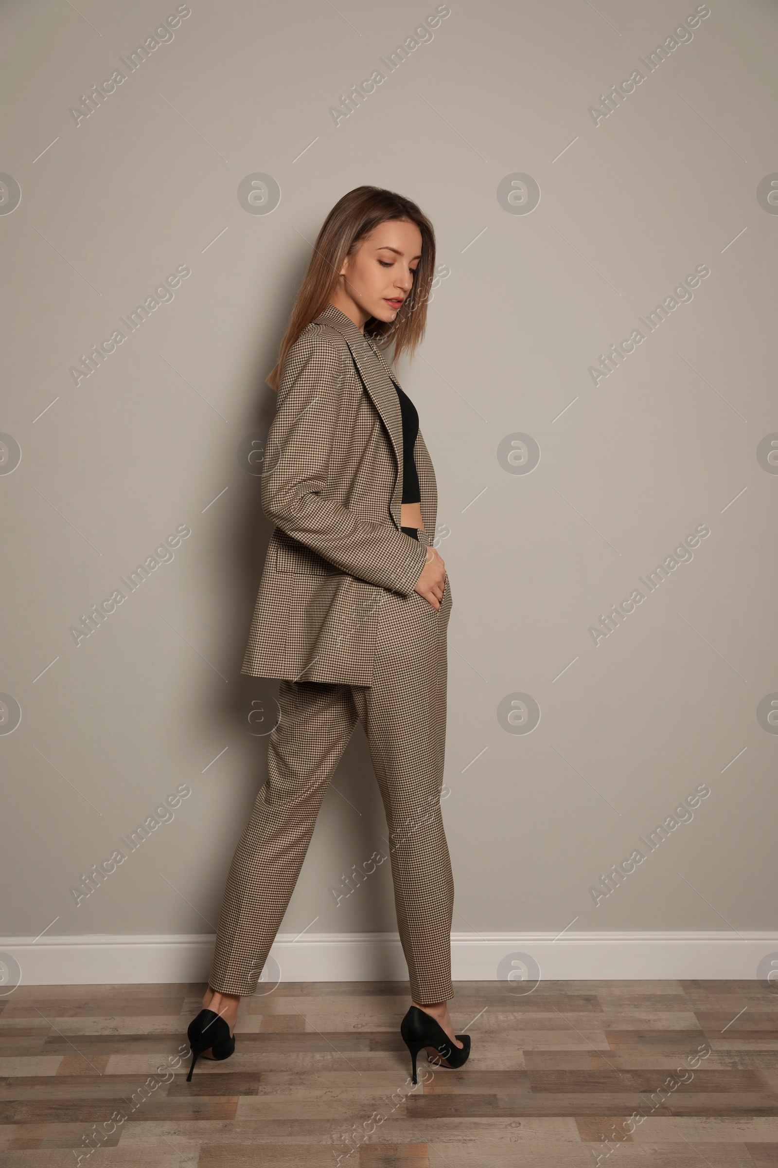Photo of Full length portrait of beautiful young woman in fashionable suit near grey wall indoors. Business attire