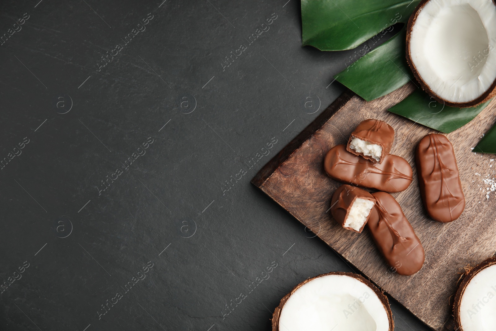 Photo of Delicious milk chocolate candy bars with coconut filling on black table, flat lay. Space for text