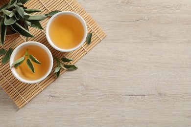 Photo of Aromatic sage tea and fresh leaves on wooden table, flat lay. Space for text