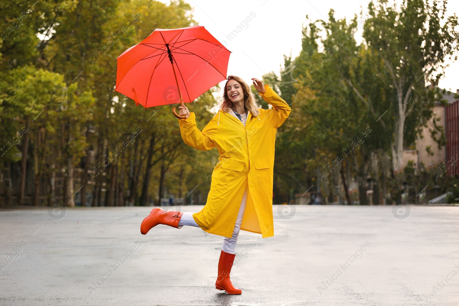 Photo of Happy young woman with red umbrella wearing yellow raincoat on street