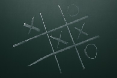 Photo of Tic tac toe game on green chalkboard, top view