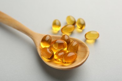 Photo of Vitamin capsules in wooden spoon on light grey background, closeup. Health supplement