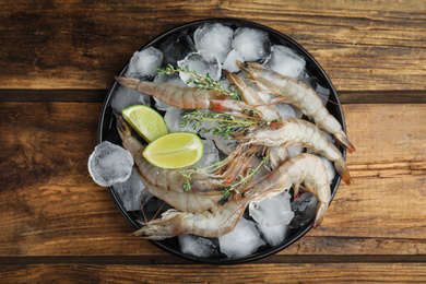 Photo of Fresh raw shrimps with ice on wooden table, top view