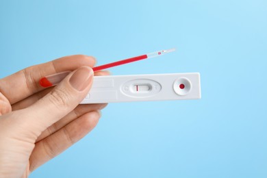 Photo of Woman holding disposable express test for hepatitis and pipette with blood on light blue background, closeup