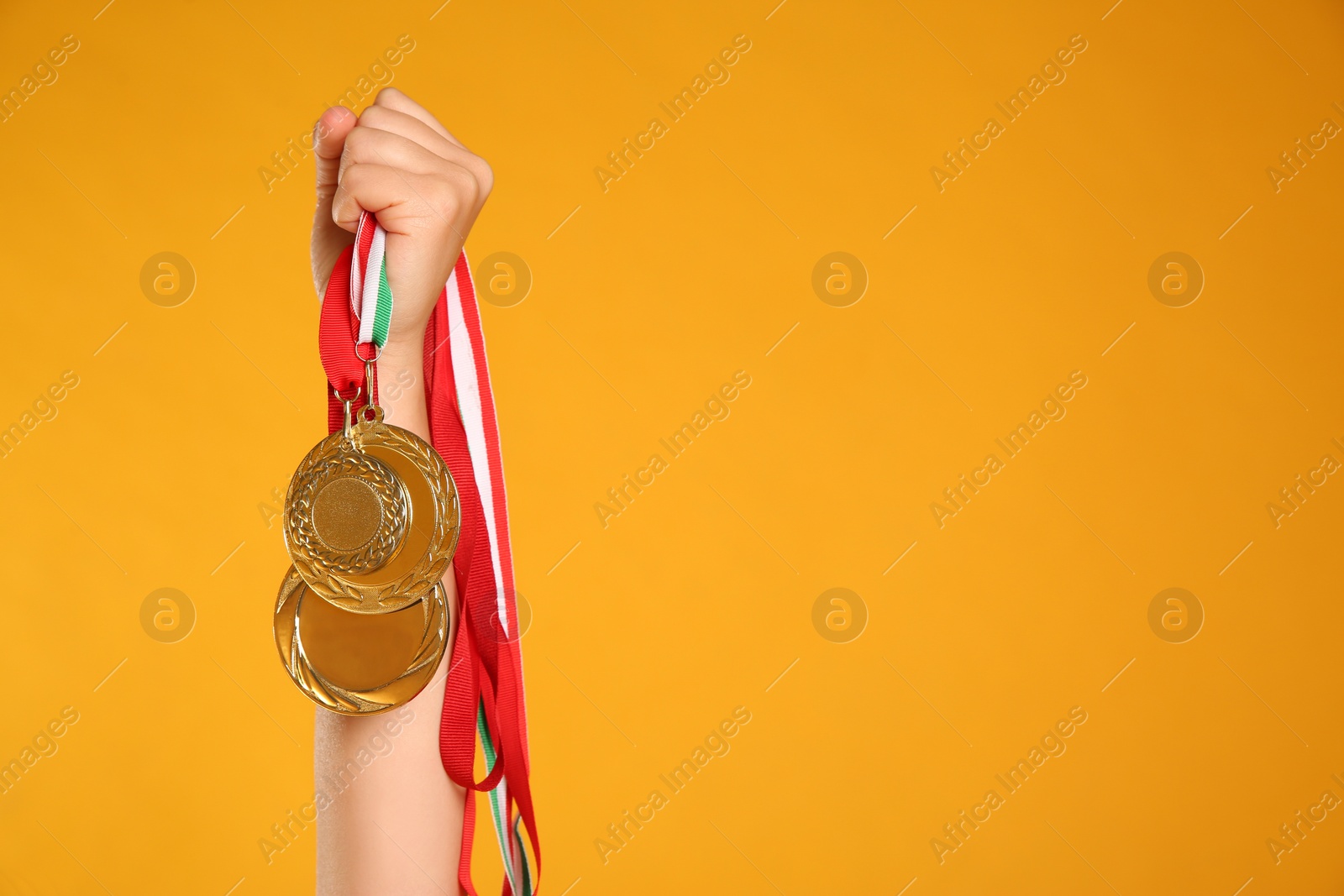 Photo of Woman holding gold medals on yellow background, closeup. Space for text