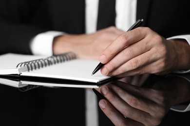 Man writing in notebook at black table, closeup