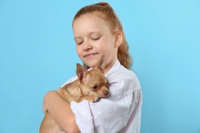 Photo of Cute little child with her Chihuahua dog on light blue background. Adorable pet