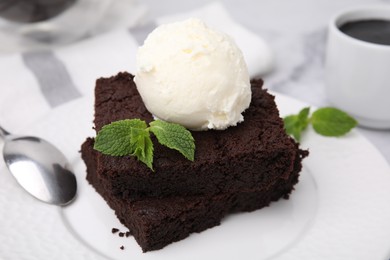 Photo of Tasty brownies served with ice cream and mint on table, closeup