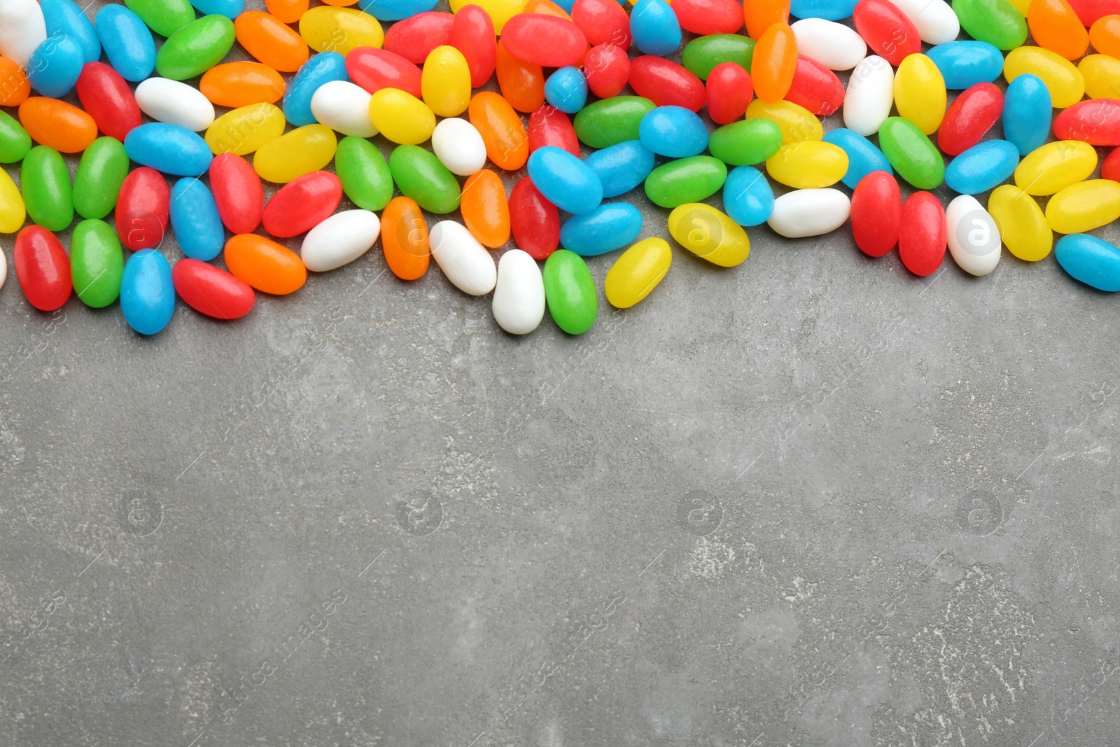 Photo of Colorful jelly beans on grey background, flat lay. Space for text