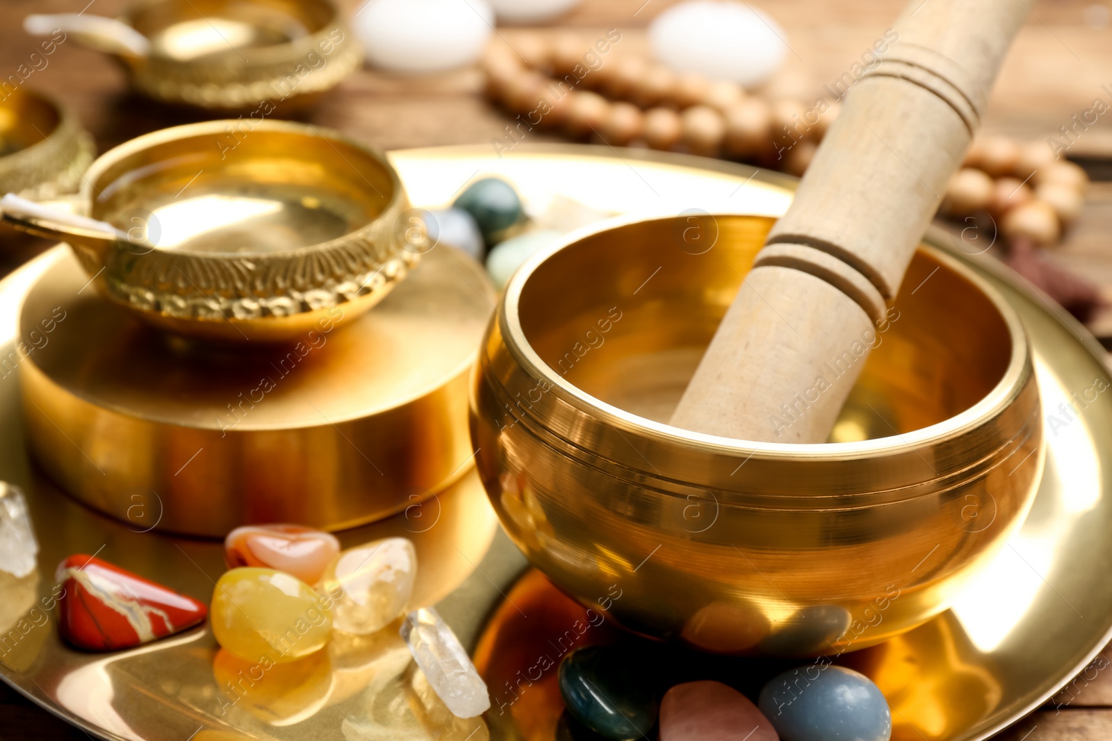 Photo of Golden singing bowl with mallet and healing stones on tray, closeup