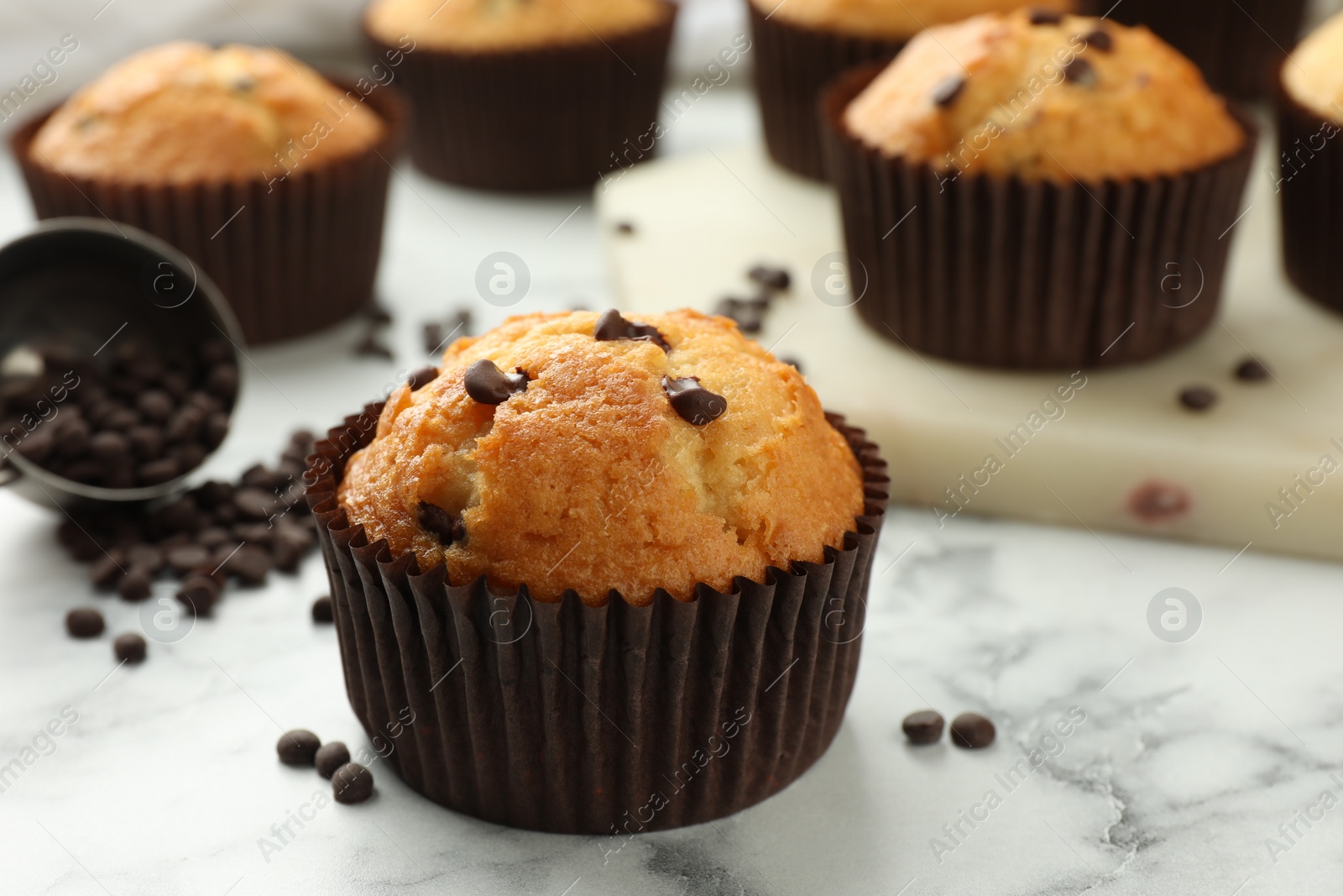 Photo of Delicious sweet muffins with chocolate chips on white marble table, closeup