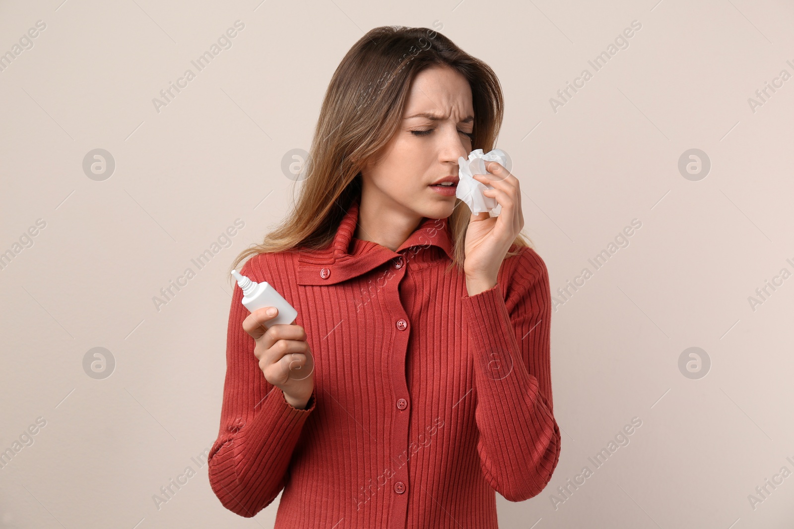 Photo of Sick young woman with nasal spray and tissue on beige background