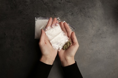 Photo of Woman holding plastic bags with cocaine, pills and hemp bud on grey background, top view