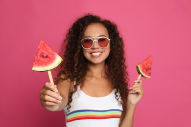 Photo of Beautiful young African American woman with pieces of watermelon against crimson background, focus on hand