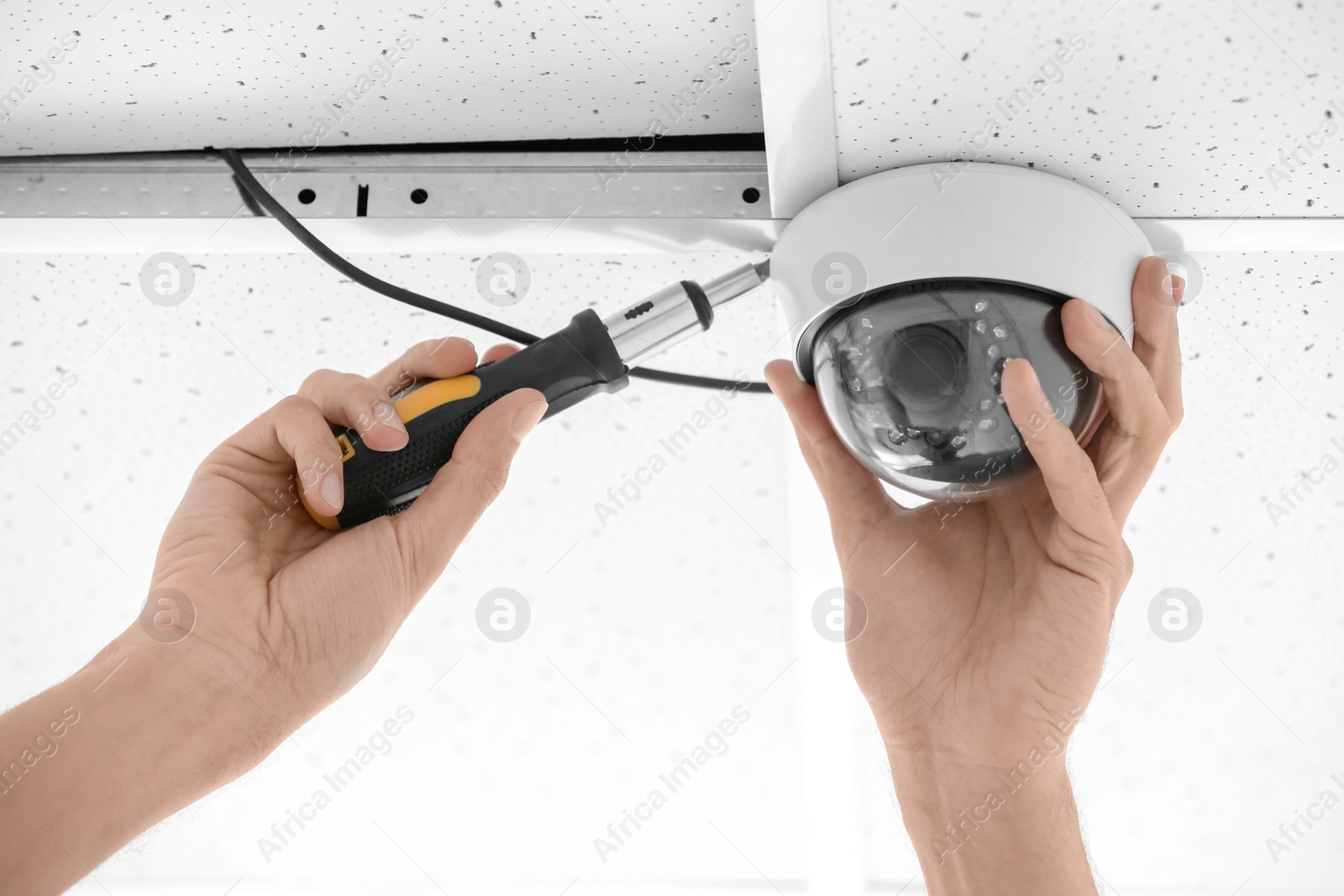 Photo of Technician installing CCTV camera on ceiling indoors, closeup