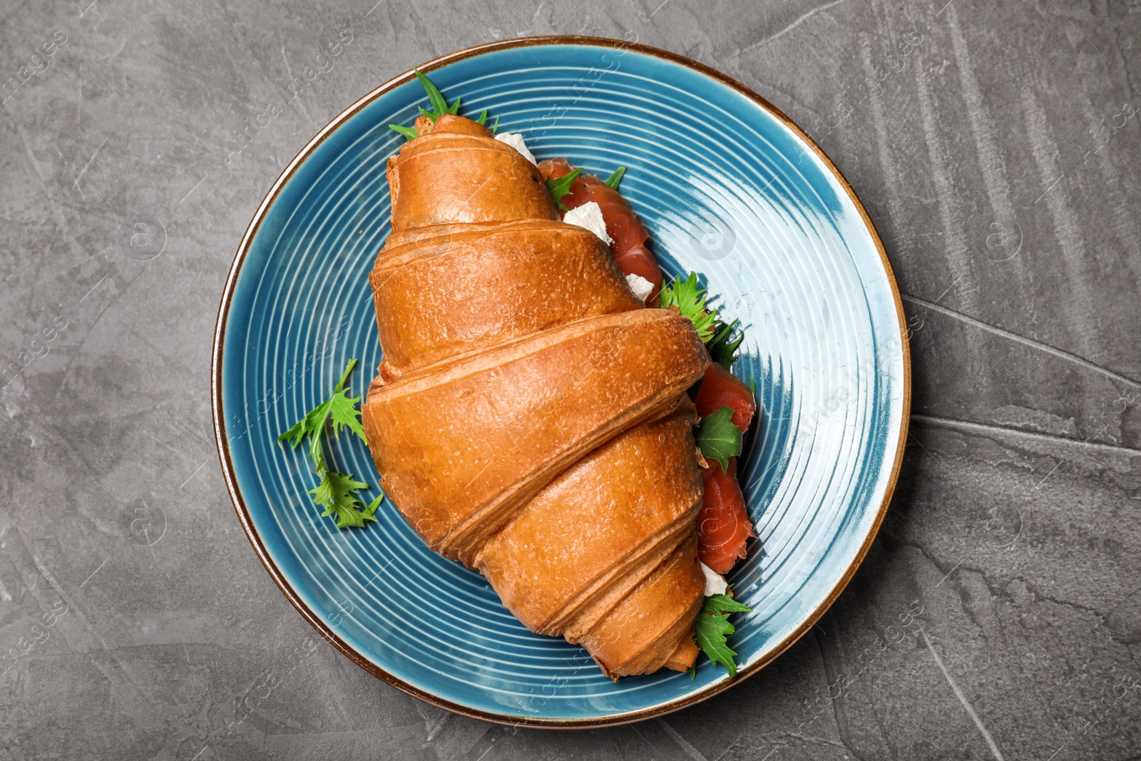 Photo of Tasty croissant sandwich with red fish on grey table, top view