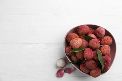 Photo of Fresh ripe lychees in bowl on white wooden table, flat lay. Space for text