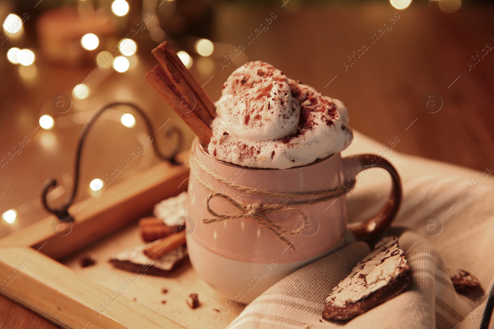 Photo of Tasty hot drink with whipped cream and Christmas lights on table, closeup