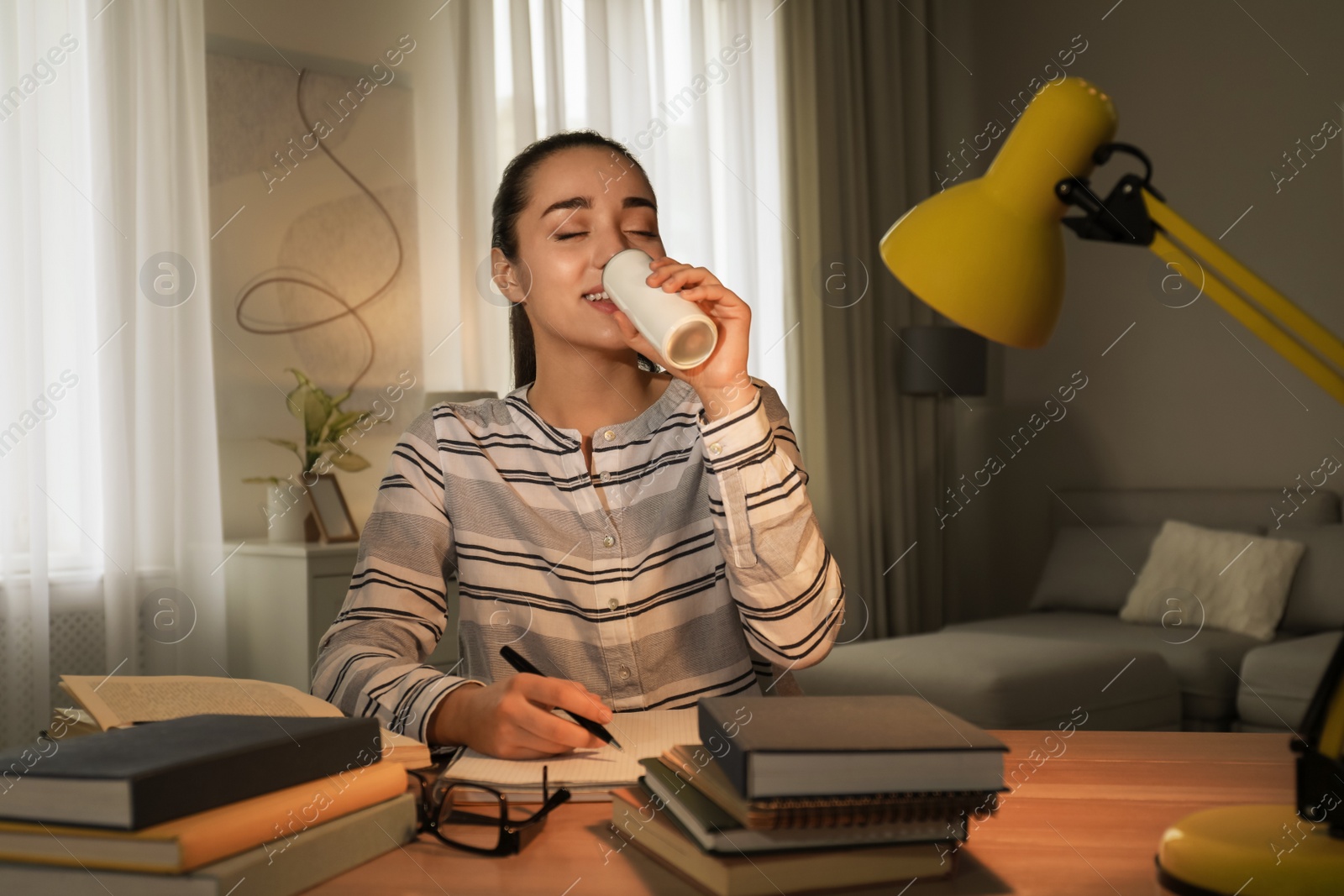 Photo of Young woman with energy drink studying at home