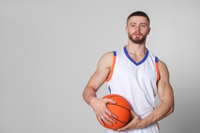 Photo of Athletic young man with basketball ball on light grey background. Space for text