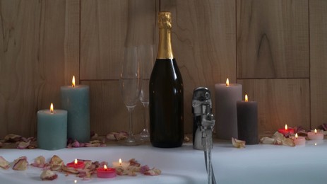 Photo of Bottle of champagne, glasses, petals and burning candles on jacuzzi in bathroom