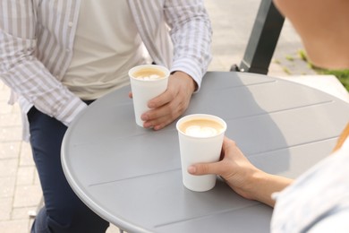 Coffee to go. Couple with paper cups at grey table outdoors, closeup