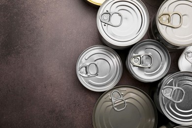 Photo of Many closed tin cans on brown table, flat lay. Space for text