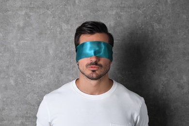 Photo of Young man wearing light blue blindfold on grey background