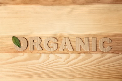 Photo of Word "Organic" madecardboard letters and green leaf on wooden background, top view