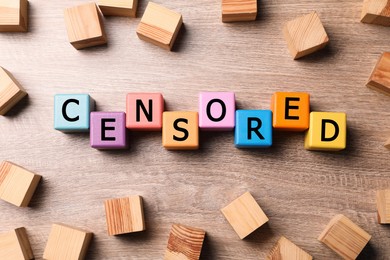 Colorful cubes with word Censored on wooden table, flat lay