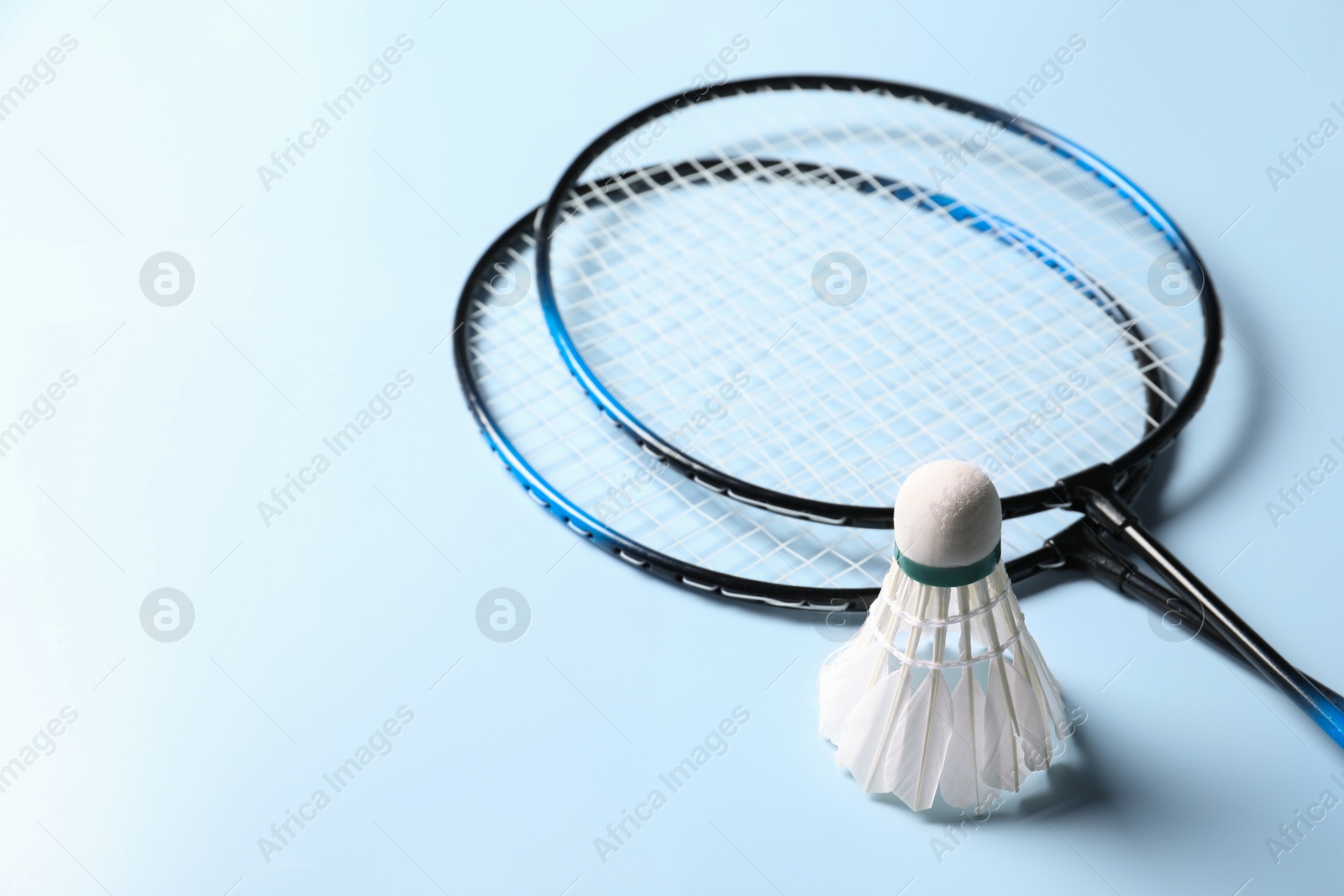 Photo of Feather badminton shuttlecock and rackets on light blue background, closeup. Space for text