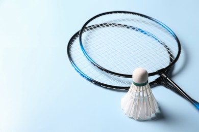 Photo of Feather badminton shuttlecock and rackets on light blue background, closeup. Space for text