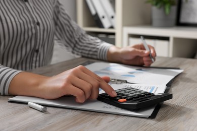 Woman using calculator at light wooden table in office, closeup