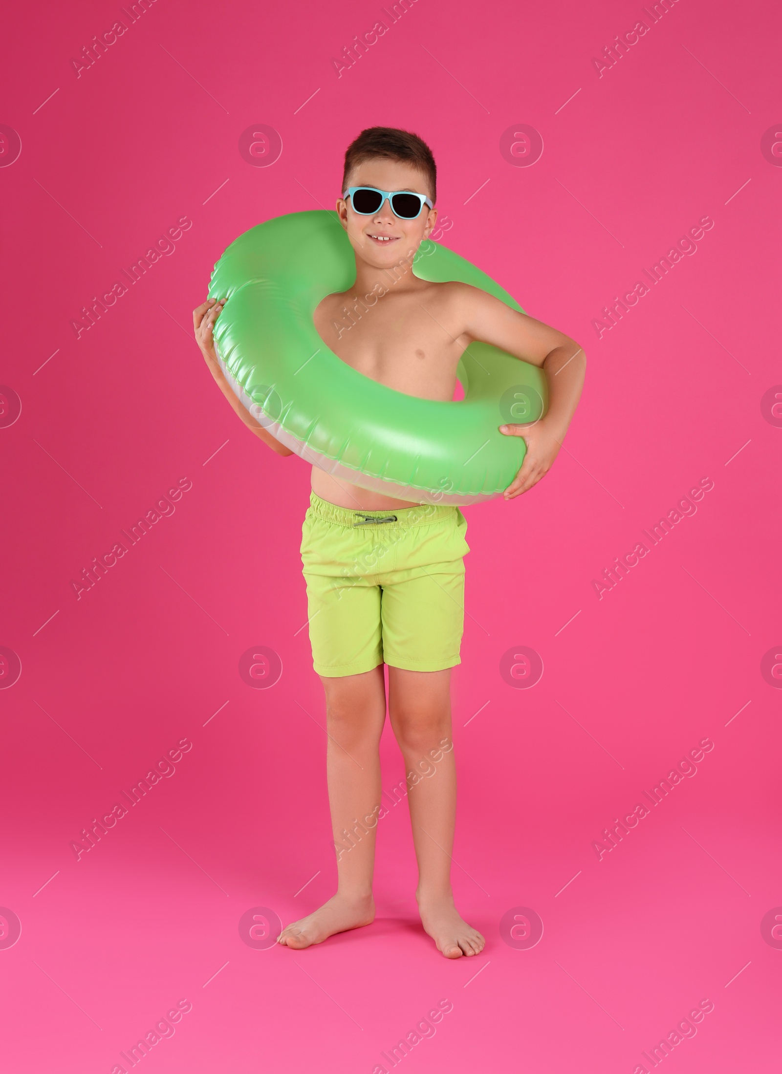 Photo of Cute little child in beachwear with bright inflatable ring on pink background